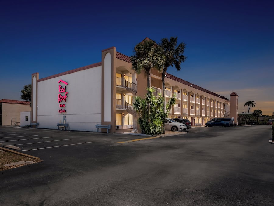 A hotel with a large sign reading "Red Roof" and a parking lot with several cars.