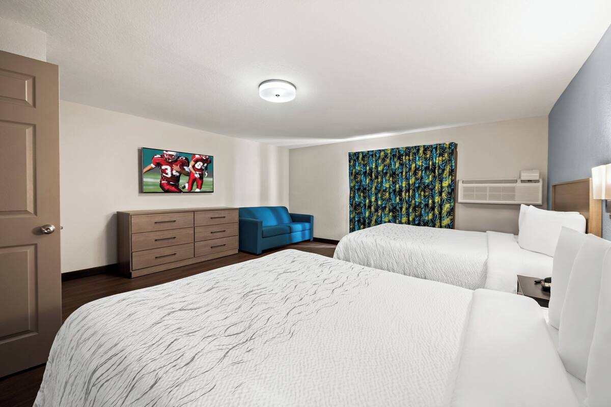 Een hotelkamer met twee bedden, een blauwe bank, een dressoir en een schilderij aan de muur.