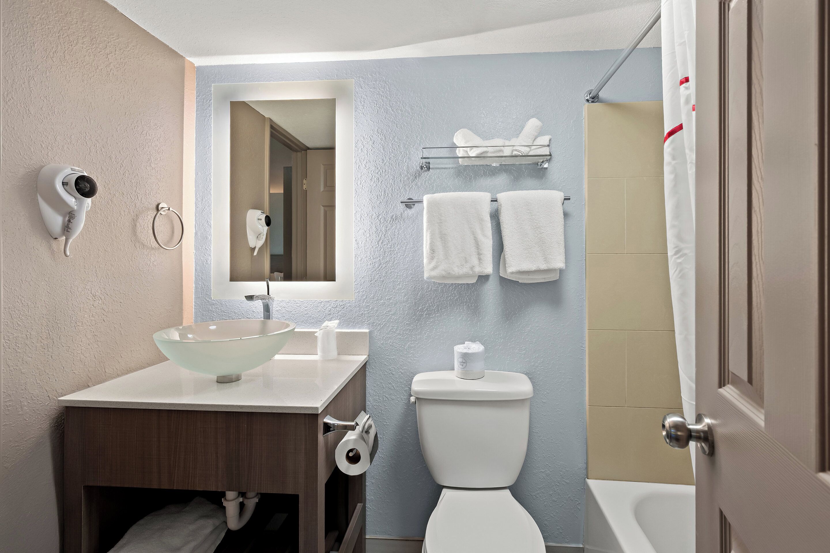 A bathroom with a glass sink, a toilet, a shower curtain, and a towel rack.