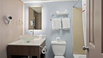 A bathroom with a glass sink, a toilet, a shower curtain, and a towel rack.
