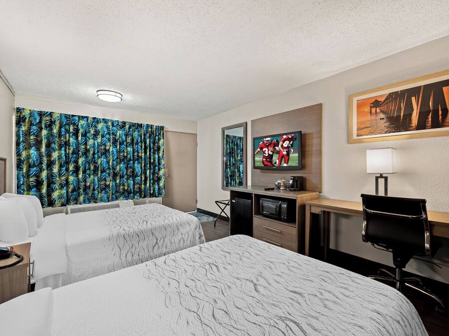 A hotel room with two beds, a desk, a chair, a TV, and a painting on the wall.