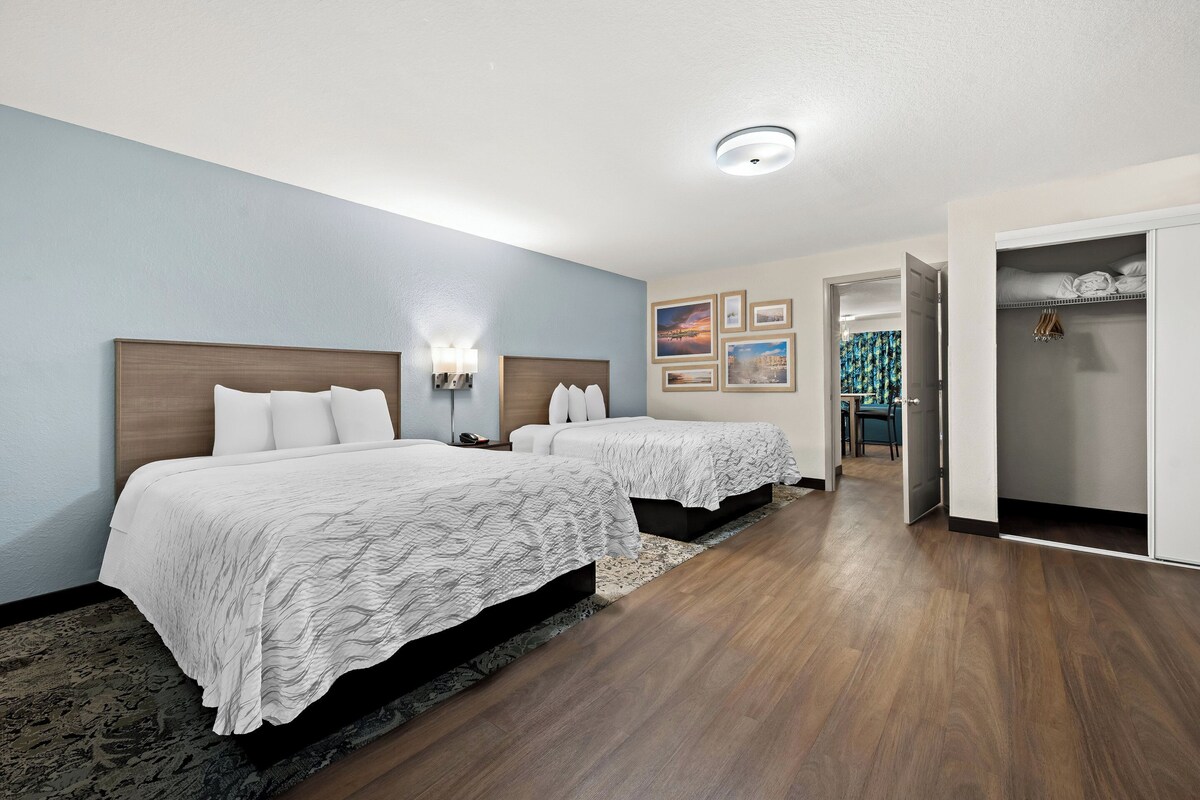 A hotel room with two beds, a wooden headboard, a wall-mounted light fixture, and a door leading to a bathroom.
