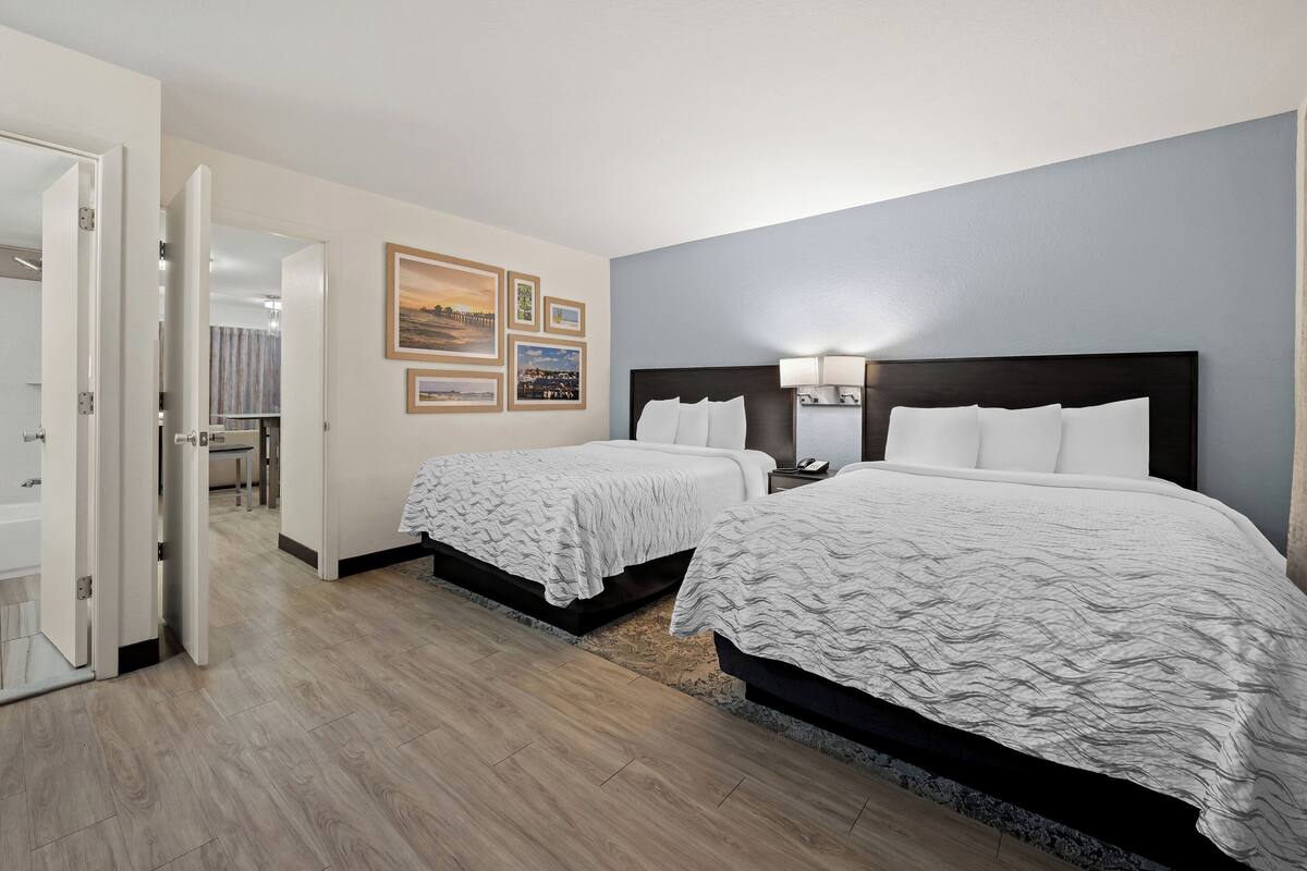 Een hotelkamer met twee bedden, een badkamer en een gang naar een andere kamer.