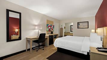 A hotel room with a bed, desk, chair, and a small kitchenette.