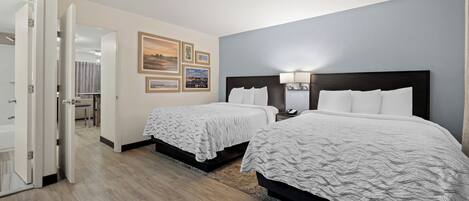 A hotel room with two beds, a bathroom, and a hallway leading to another room.