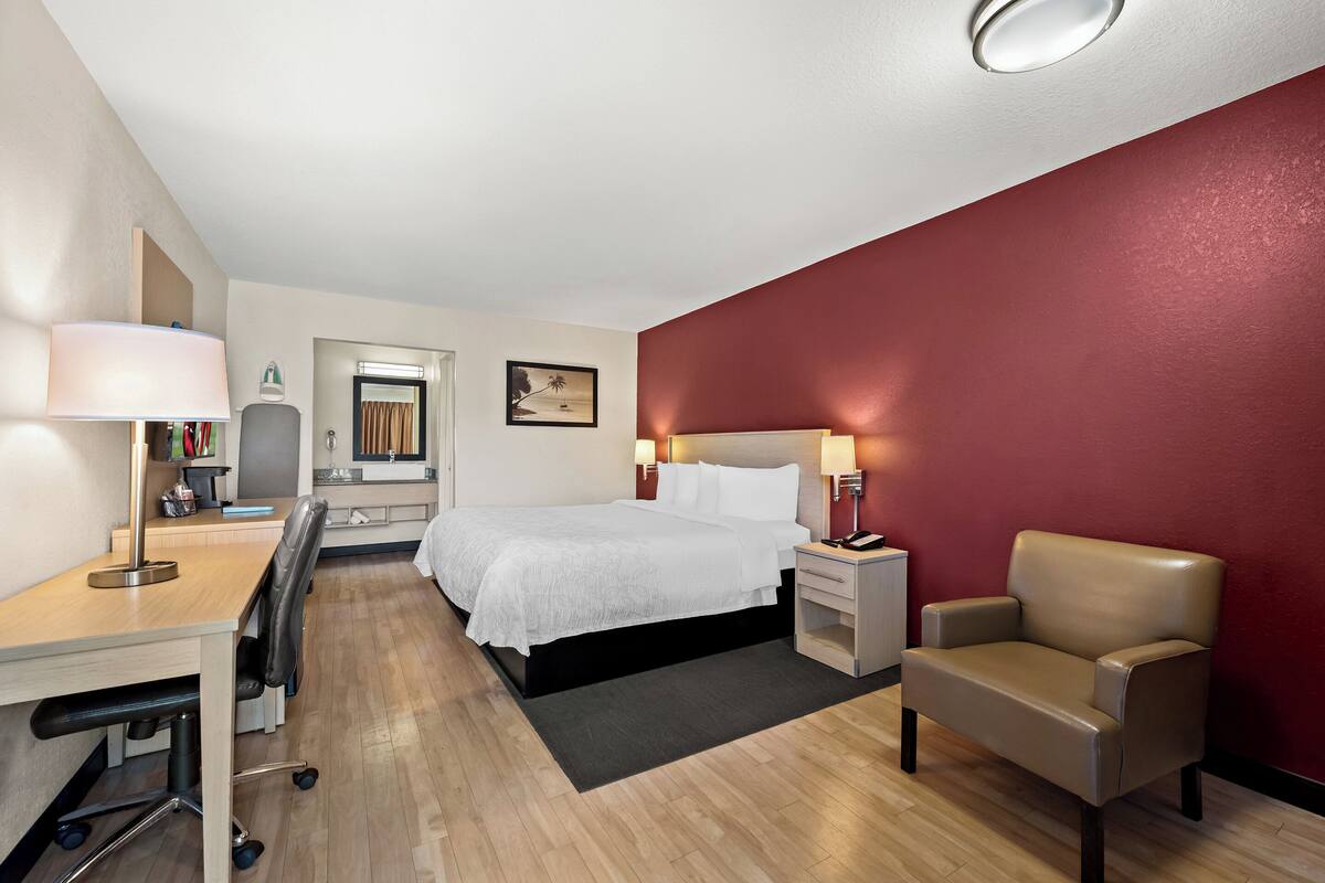 Een hotelkamer met een bed, bureau, stoel en een rode accentmuur.