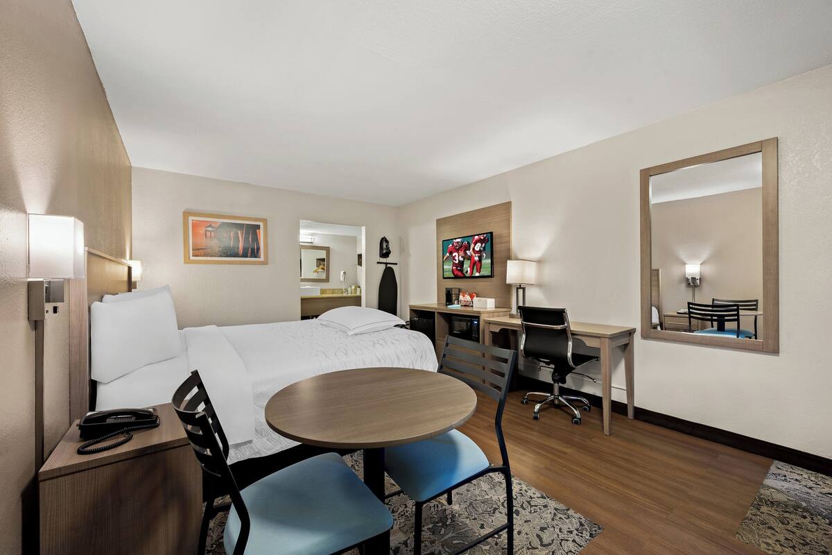 Een hotelkamer met een bed, bureau, stoel en een klein tafeltje.