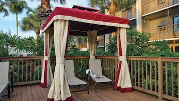 Un espace extérieur aménagé, abrité et doté de deux fauteuils et d’une table, entouré d’une terrasse en bois et de palmiers.