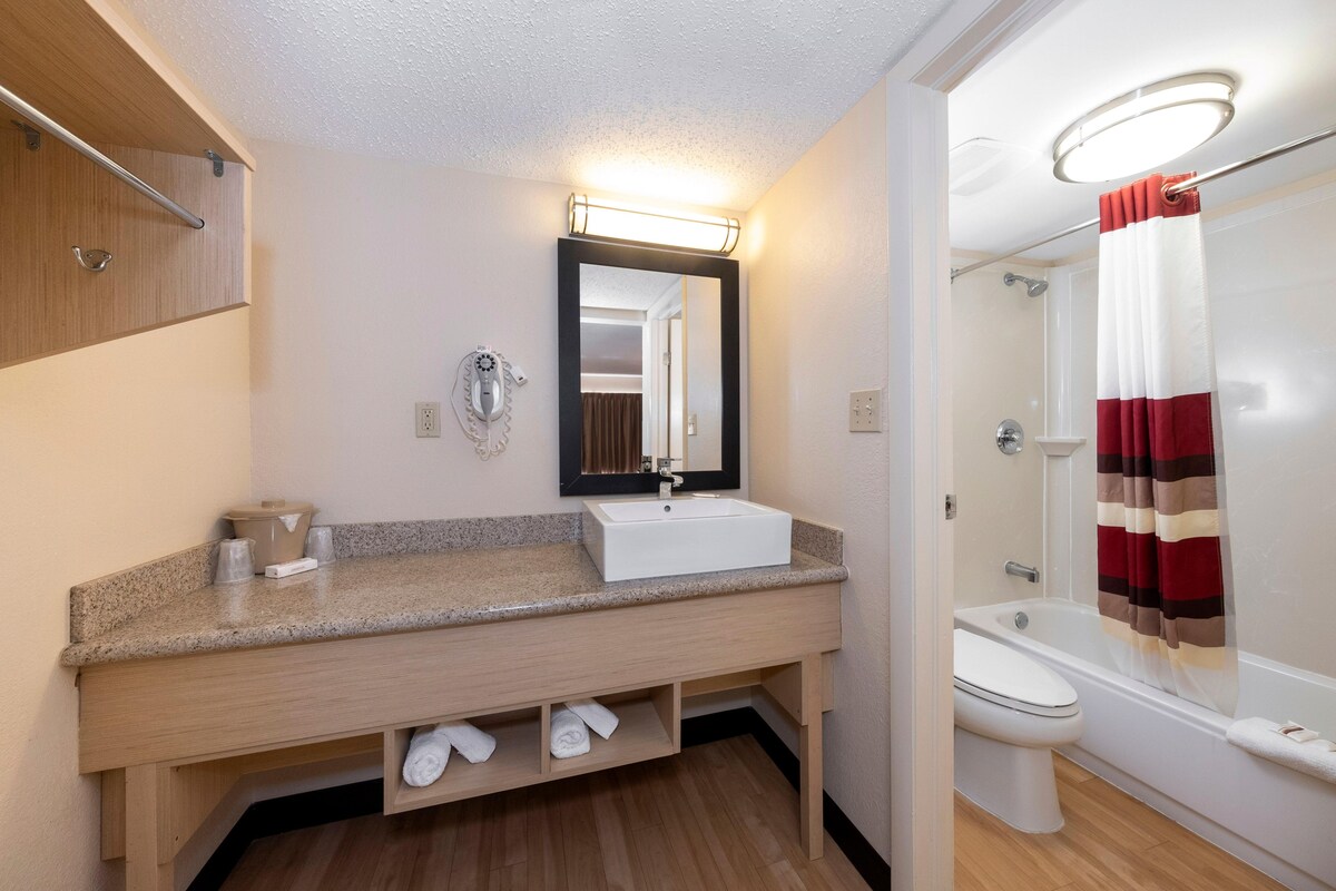A modern bathroom with a granite countertop sink, a mirror, a shower with a striped curtain, and a toilet.