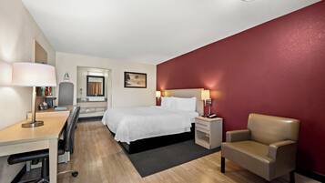 Habitación de hotel con cama, escritorio, silla y una pared de acento roja.
