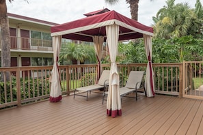 A wooden deck with a canopy and two lounge chairs.