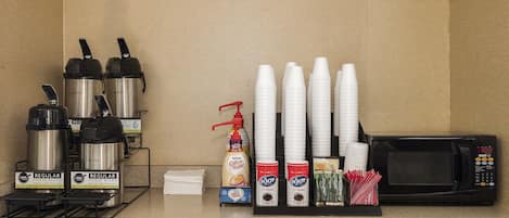 A coffee station with coffee makers, disposable cups, and a microwave.