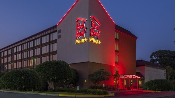Un edificio moderno con un techo rojo característico y señalización que dice 'Red Roof Plus'.
