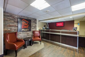 A reception area with a Red Roof Plus sign, a reception desk, two leather chairs, and a digital screen advertising free Wi-Fi. - Red Roof Inn PLUS+ Boston - Woburn/ Burlington (Woburn)