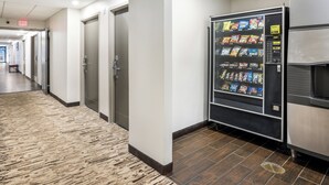 A hallway with a vending machine stocked with snacks, a bench, and an exit sign. - Red Roof Inn PLUS+ Boston - Woburn/ Burlington (Woburn)