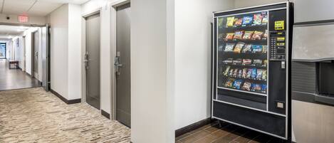A hallway with a vending machine stocked with snacks, a bench, and an exit sign.