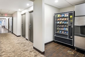 A hallway with a vending machine stocked with snacks, a bench, and an exit sign. - Red Roof Inn PLUS+ Boston - Woburn/ Burlington (Woburn)
