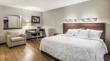 Una habitación de hotel con cama, escritorio, silla, lámpara de escritorio, un cuadro en la pared y un espejo.