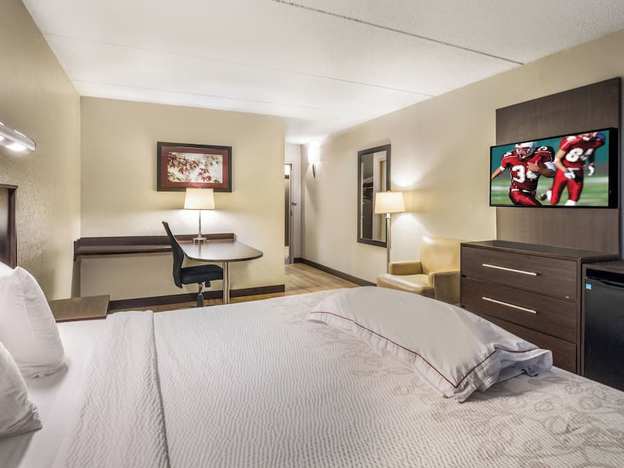 Una habitación de hotel con cama, escritorio, silla, televisor y armario.