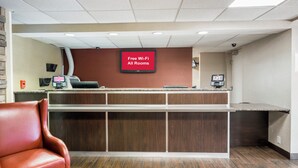 A reception area with a 'Free Wi-Fi All Rooms' sign, a reception desk, a phone, and a leather chair. - Red Roof Inn PLUS+ Boston - Woburn/ Burlington (Woburn)