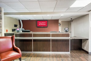 A reception area with a 'Free Wi-Fi All Rooms' sign, a reception desk, a phone, and a leather chair. - Red Roof Inn PLUS+ Boston - Woburn/ Burlington (Woburn)