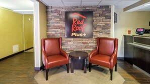 Vestíbulo de un hotel Red Roof Plus con dos sillones de cuero, una mesita y un mostrador de recepción.