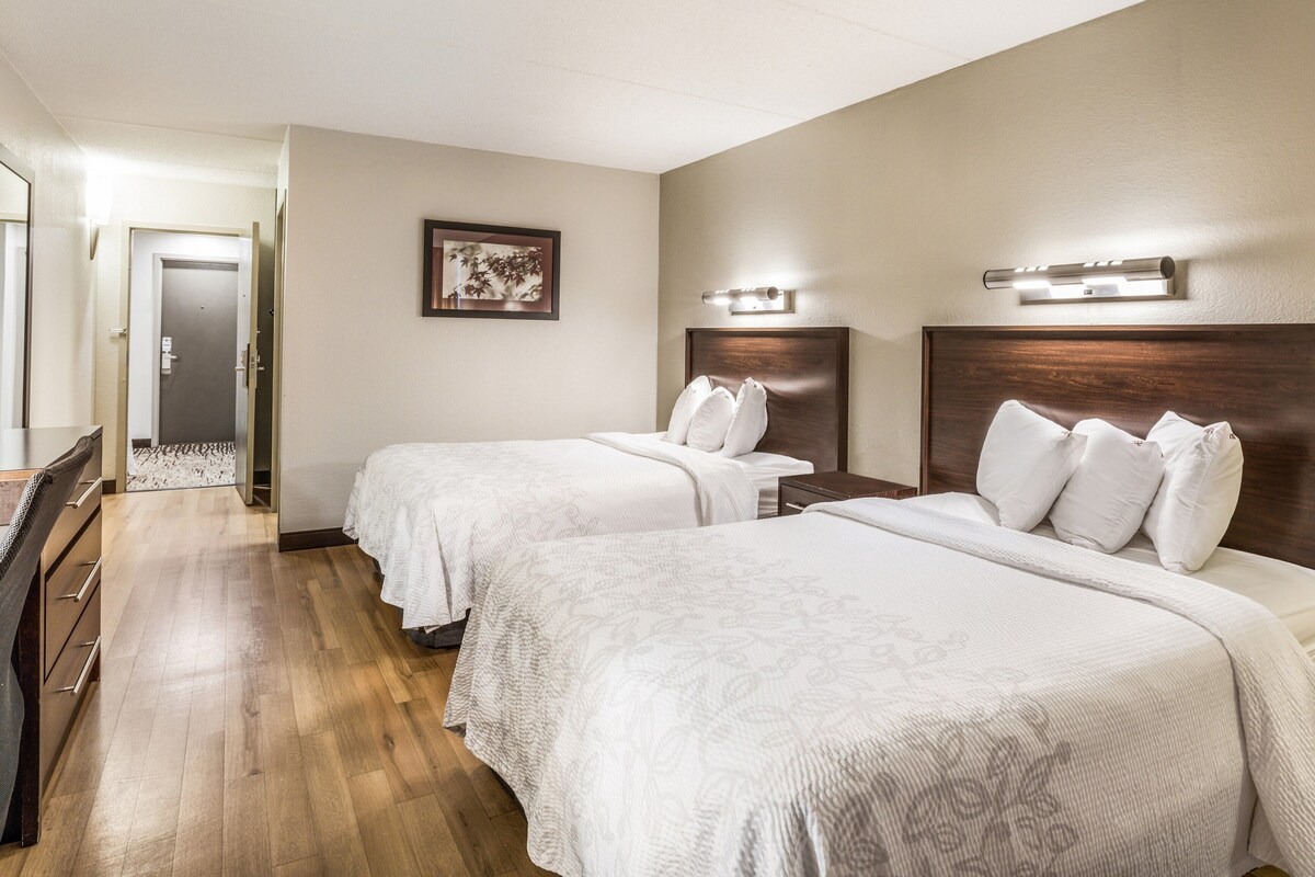 A hotel room with two beds, a desk, and a door.