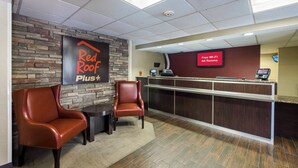 A reception area with a Red Roof Plus sign, a reception desk, two leather chairs, and a digital screen advertising free Wi-Fi. - Red Roof Inn PLUS+ Boston - Woburn/ Burlington (Woburn)