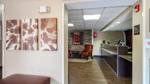 A hotel lobby with a reception desk, a Red Roof Plus sign, and a bench. - Red Roof Inn PLUS+ Boston - Woburn/ Burlington (Woburn)