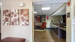 A hotel lobby with a reception desk, a Red Roof Plus sign, and a bench. - Red Roof Inn PLUS+ Boston - Woburn/ Burlington (Woburn)