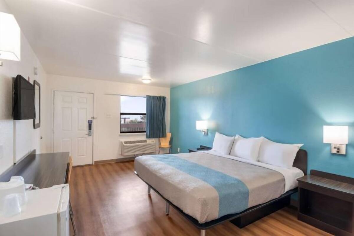 Habitación de hotel con cama, mesitas de noche, escritorio, silla, ventana con cortinas y vistas.