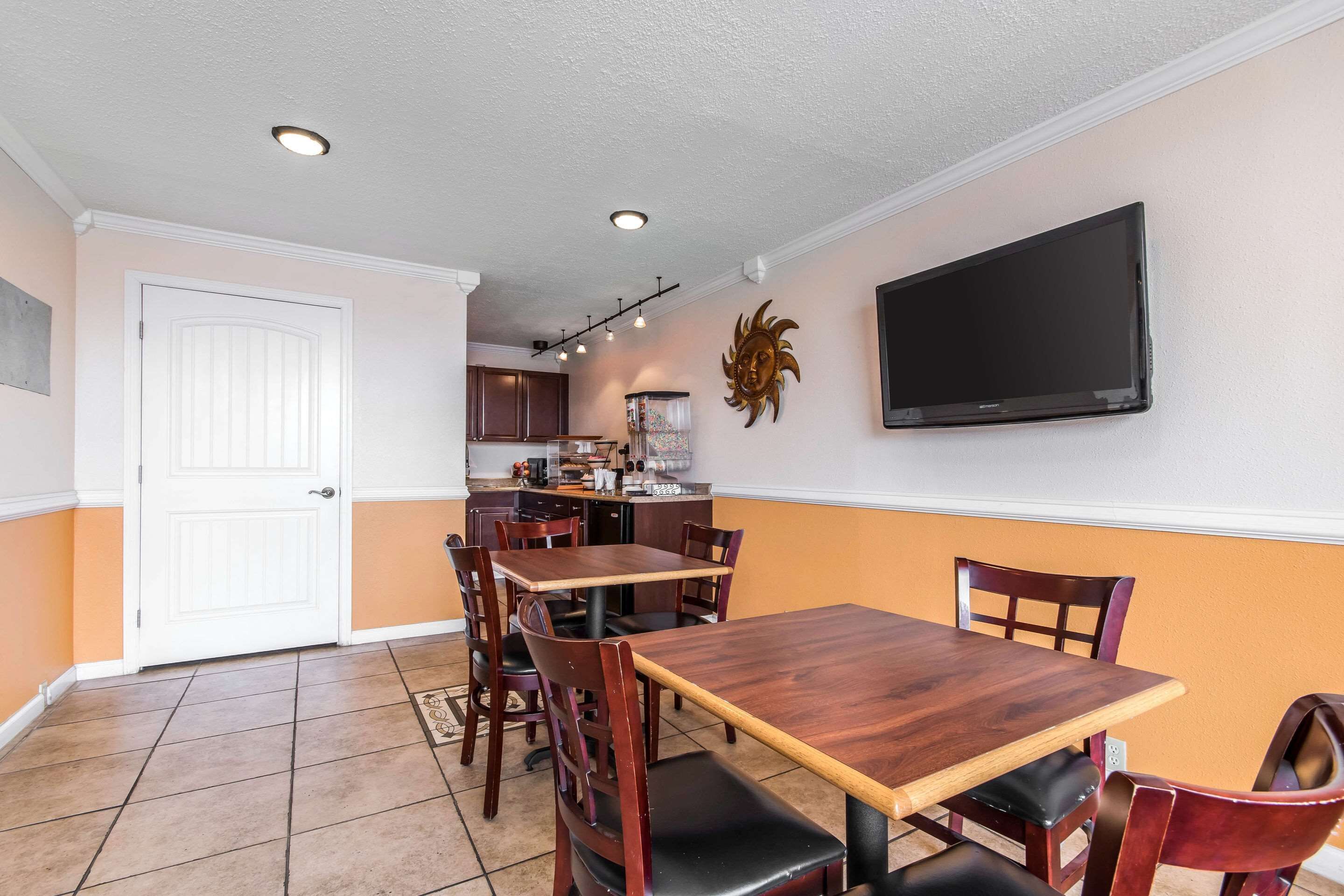 Un área de comedor con una mesa y sillas de madera, una cocina al fondo y un televisor montado en la pared.