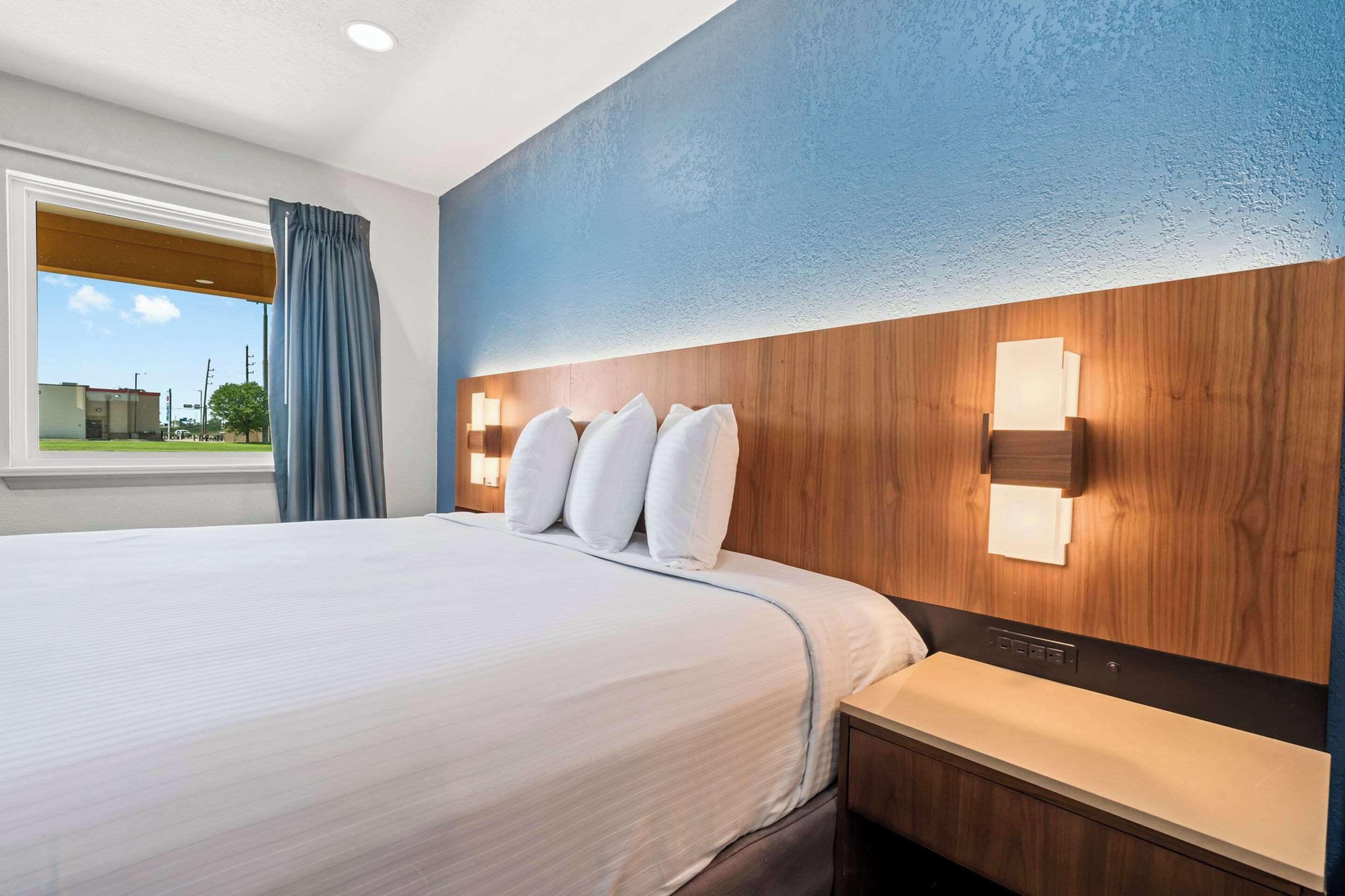 A hotel room with a large bed, a wooden headboard, and a nightstand with a lamp.
