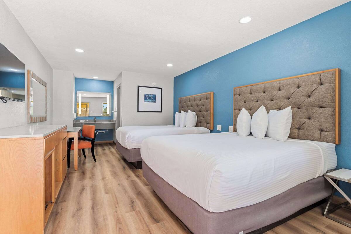A hotel room with two beds, a desk, and a chair.