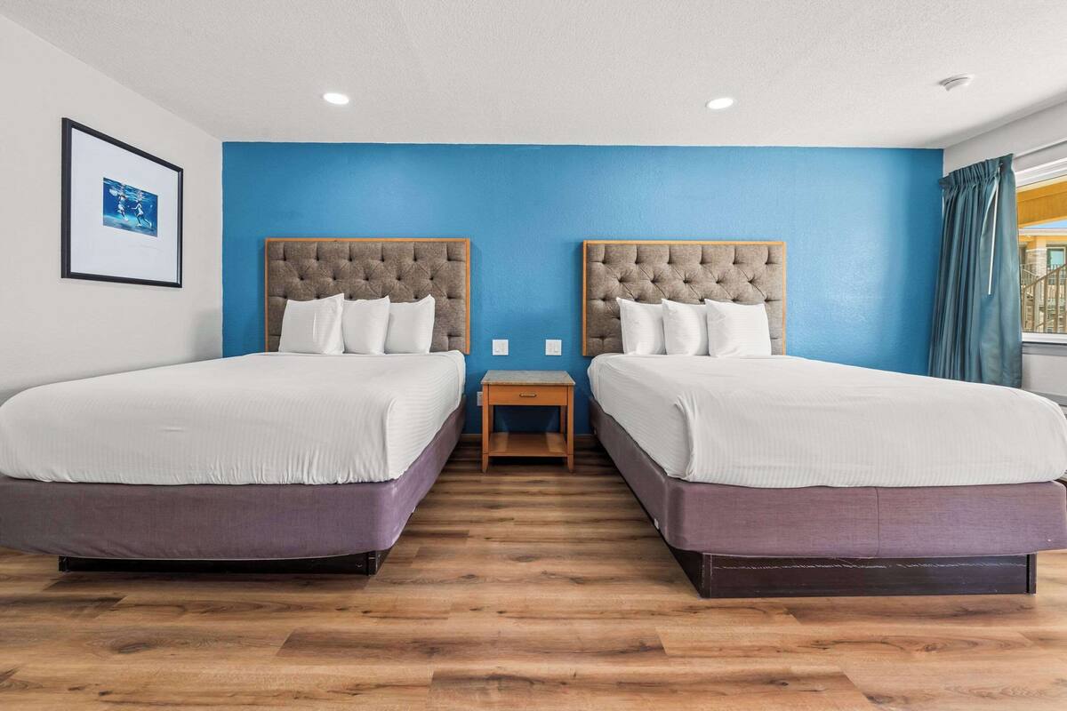 A hotel room with two beds, a wooden nightstand, and a framed picture on the wall.