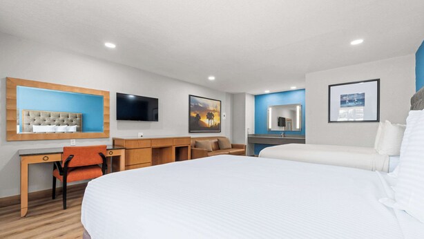 A hotel room with a large bed, a desk with a chair, a sofa, a TV mounted on the wall, and artwork on the walls. - Econo Lodge Inn & Suites Sealy (Sealy)