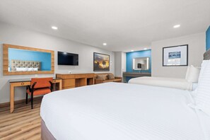 A hotel room with a large bed, a desk with a chair, a sofa, a TV mounted on the wall, and artwork on the walls. - Econo Lodge Inn & Suites Sealy (Sealy)