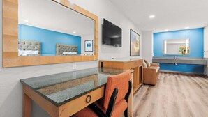 A modern hotel room with a large bed, a desk with a chair, a TV, and a bathroom with a blue wall and a large mirror. - Econo Lodge Inn & Suites Sealy (Sealy)