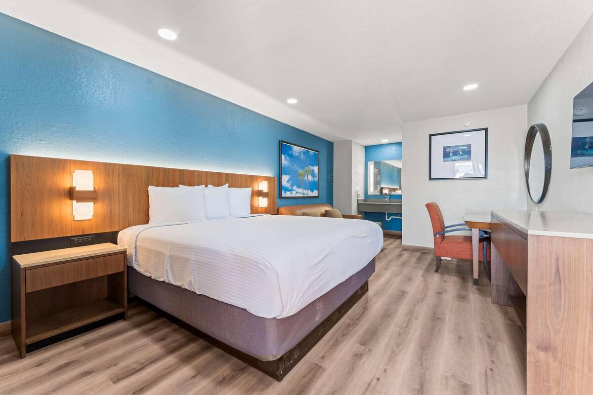 A hotel room with a large bed, a desk, a chair, and a mirror.