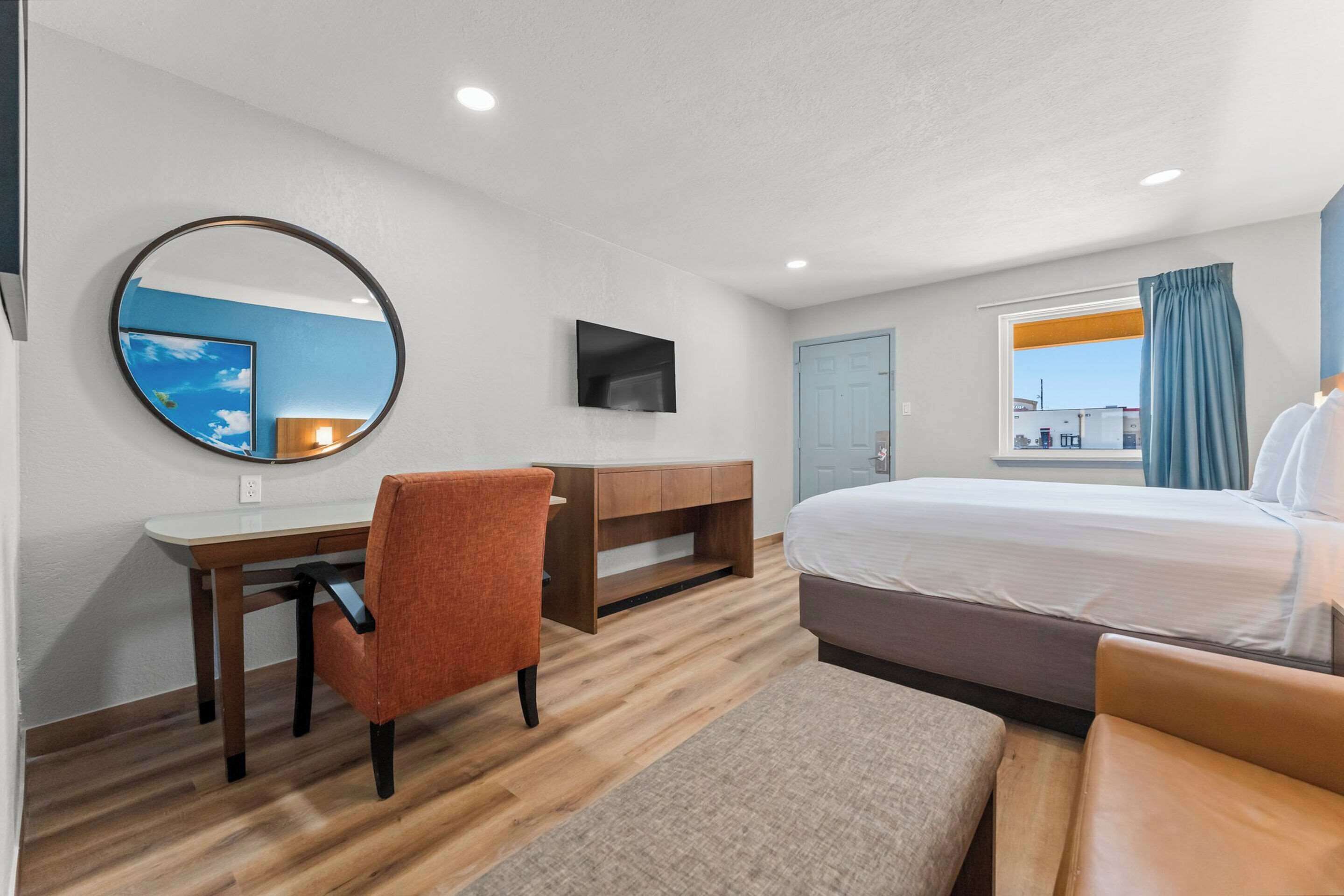 A hotel room with a bed, a desk with a chair, a television, and a window with curtains.