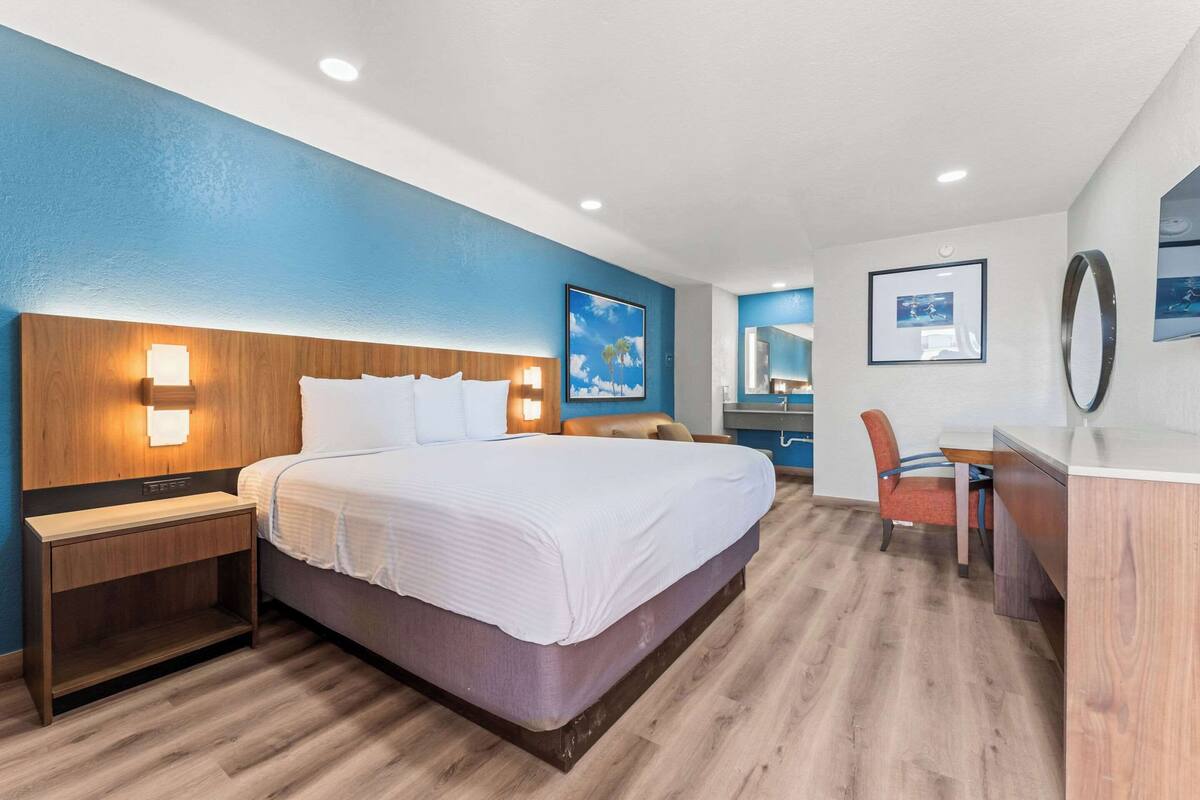 A hotel room with a large bed, wooden headboard, bedside table, and a desk with a chair.