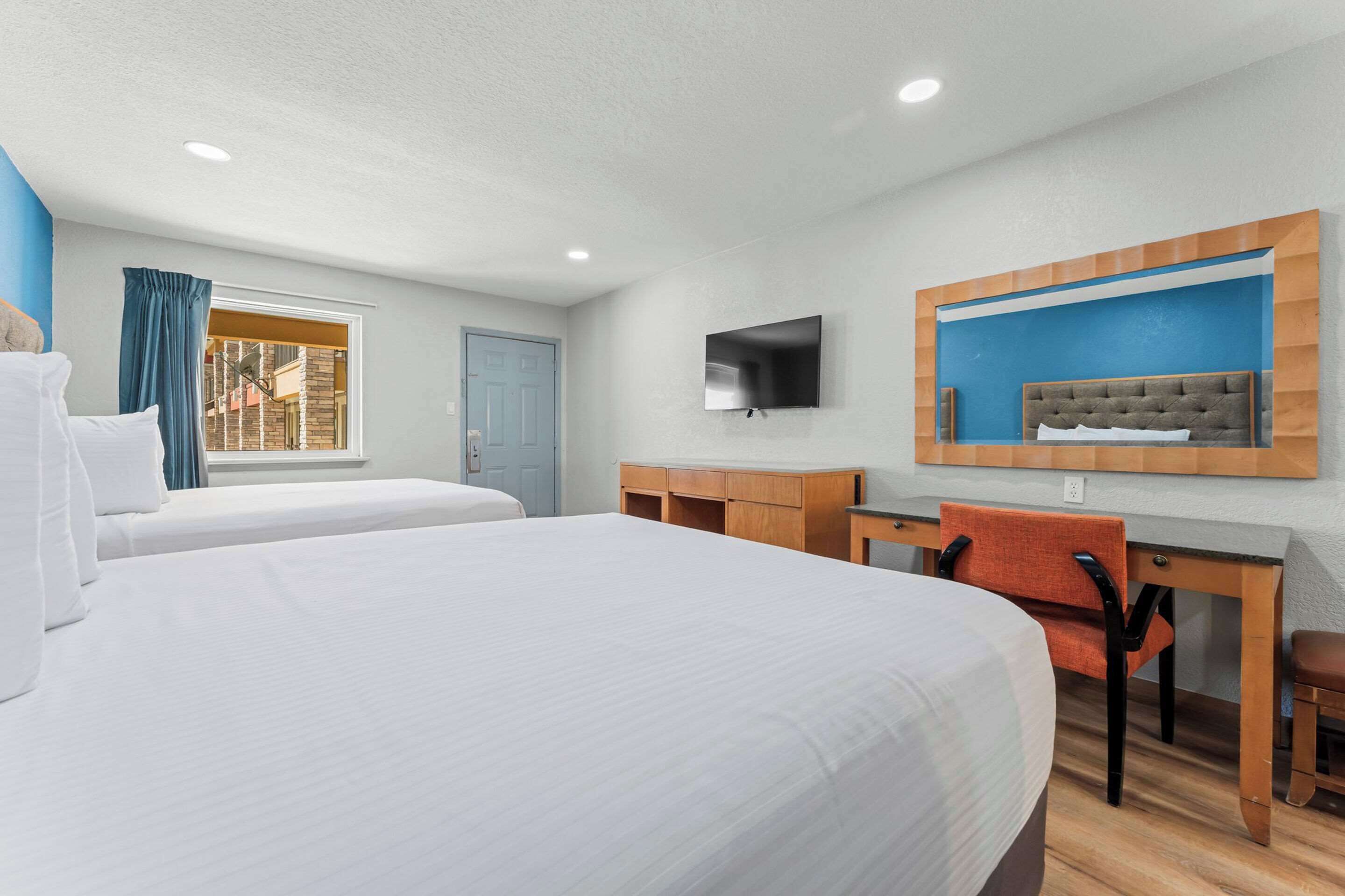 A hotel room with two beds, a desk, a chair, a television, and a window with curtains.