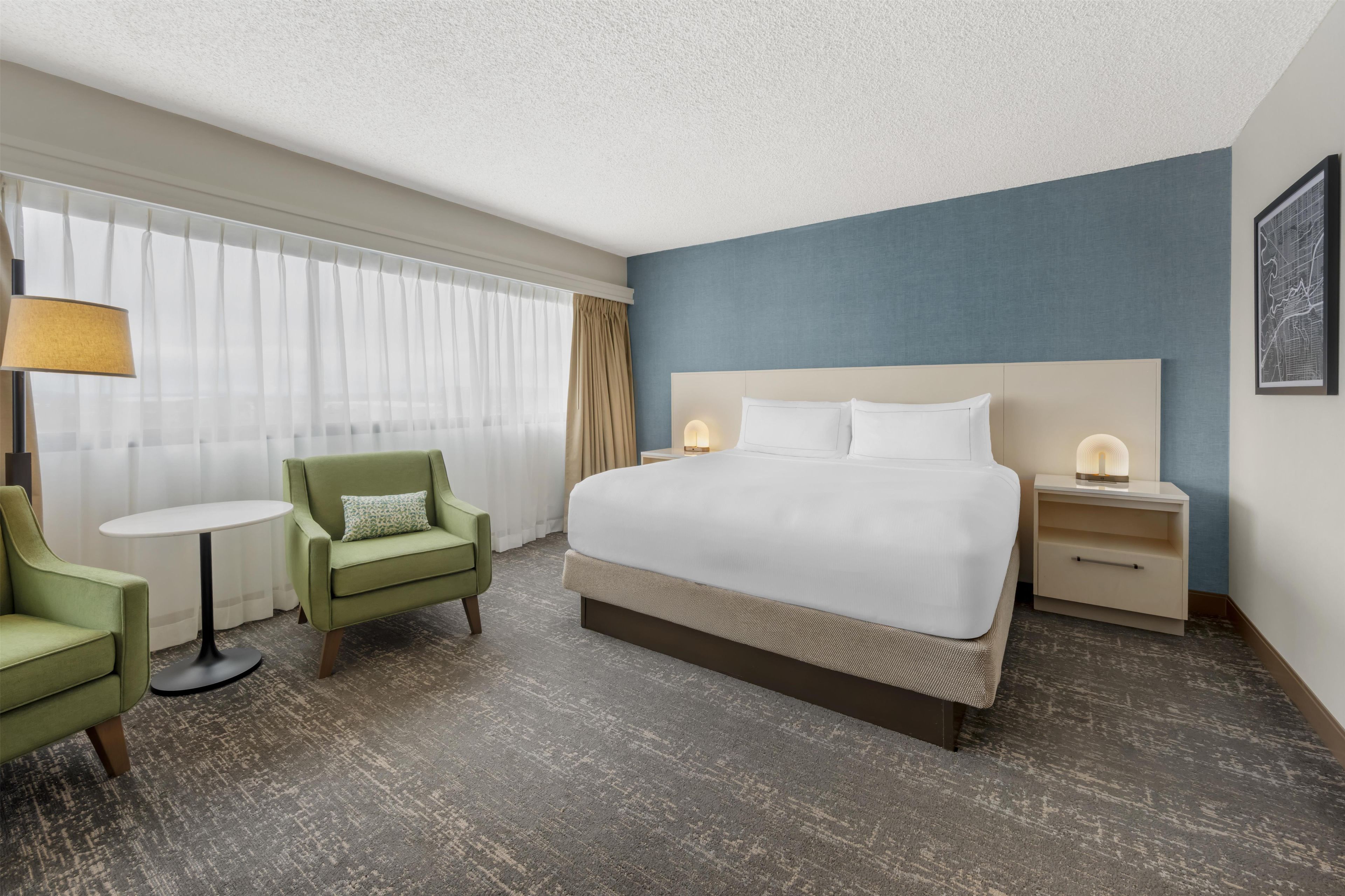A hotel room with a bed, a chair, a table, and a nightstand.
