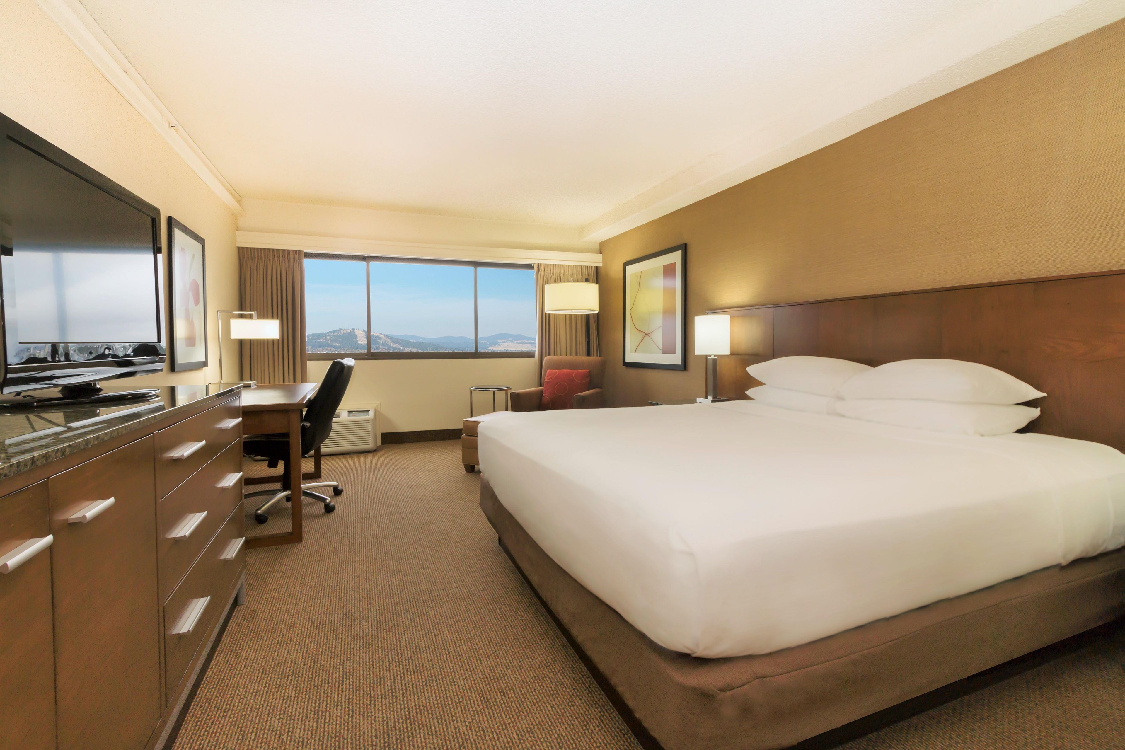 A hotel room with a bed, a desk, a chair, a TV, and a window with a view.