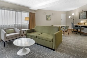A hotel room with a green sofa, a white armchair, a small round table, a dining table with chairs, and a desk with a lamp. - DoubleTree by Hilton Spokane City Center (Spokane)