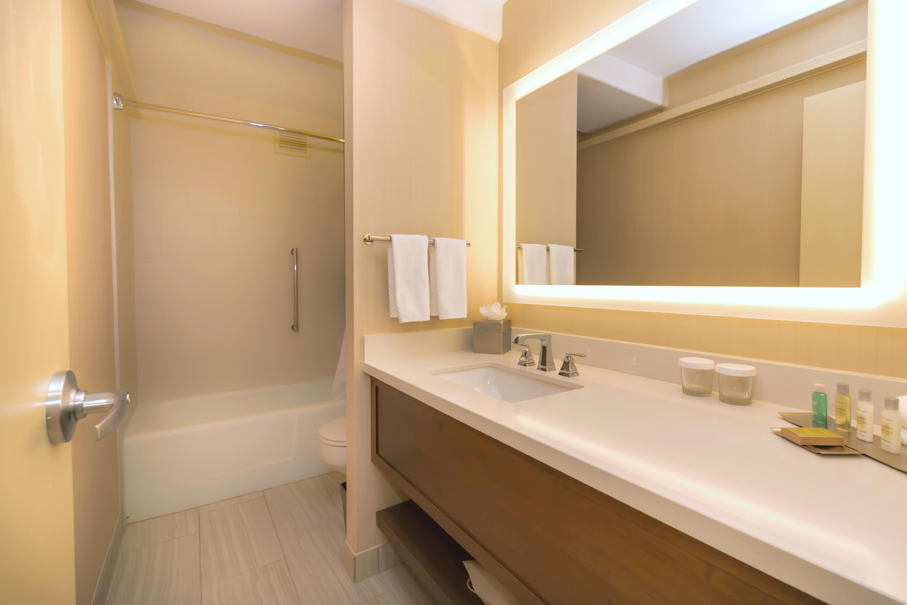 A bathroom with a bathtub, a sink, a mirror, and toiletries on the counter.
