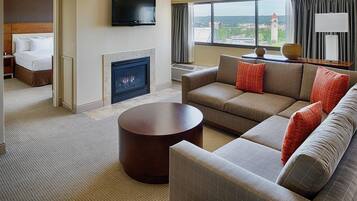 A hotel room with a sofa, a round coffee table, a fireplace, a television, and a view of a tower through the window.