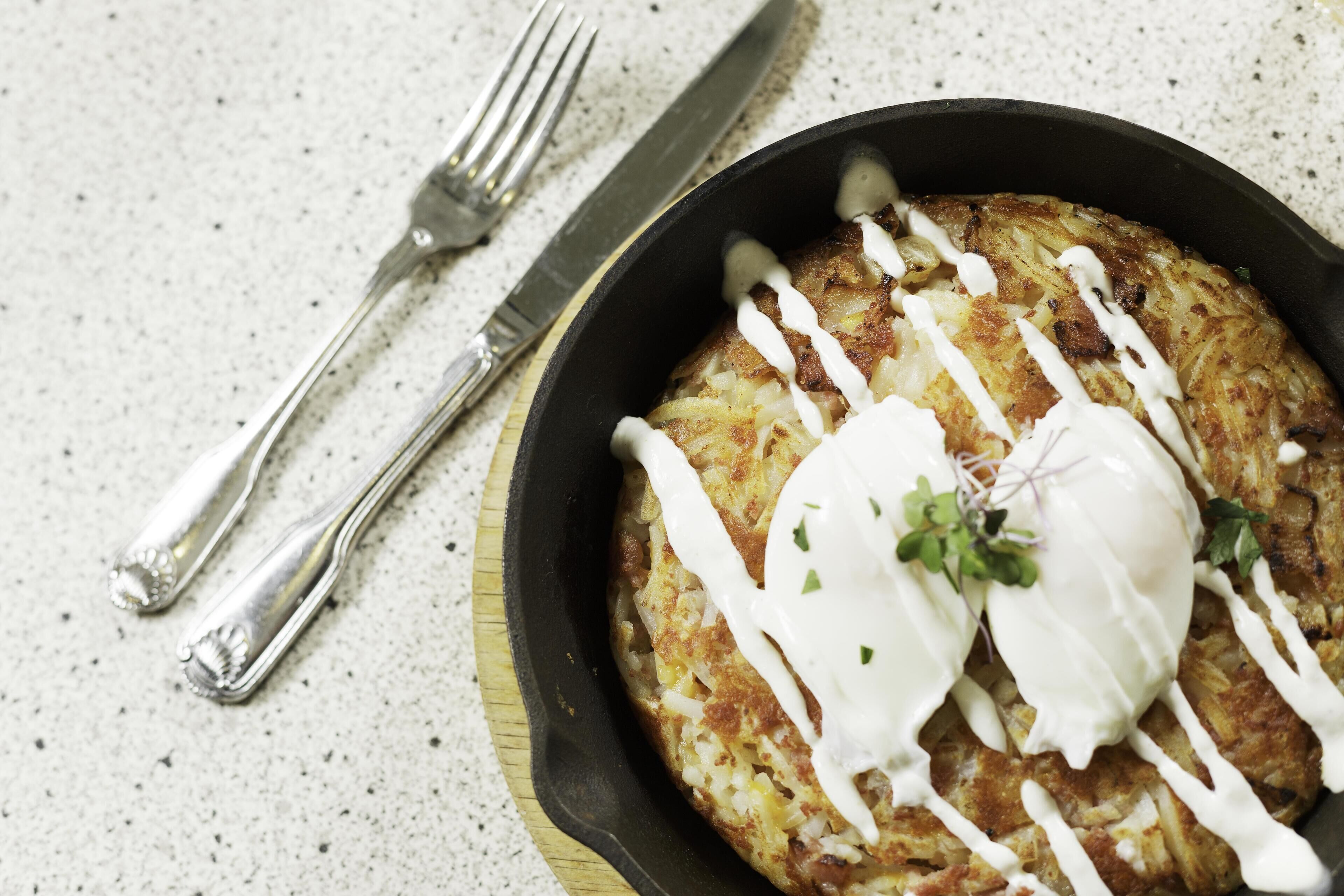 A skillet with a potato dish, a fork, and a knife on a table.