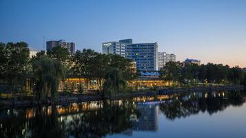 Un hotel junto al agua, con su reflejo en el lago, rodeado de árboles y otros edificios.