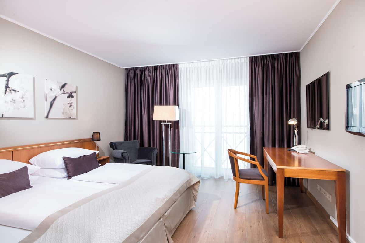 Hotellihuone, jossa on sänky, työpöytä, tuoli, lamppu ja taideteos seinällä.